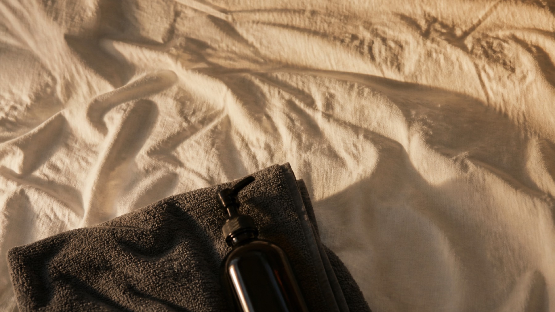 Close-up of a massage table with linen, oil bottle and folded cloth in warm light